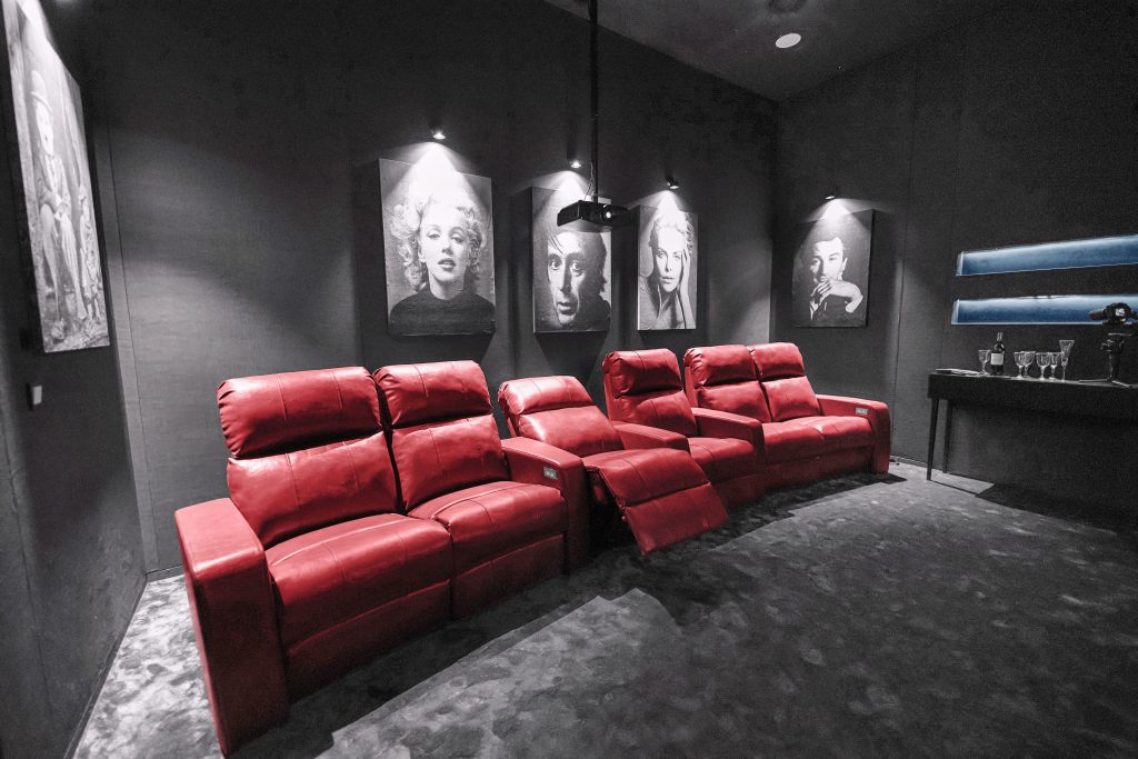 تصویری از سینما خانگی با صندلی‌های راحتی قرمز، نمایش فیلم از یک صفحه نمایش بزرگ و دکوراسیون مدرن.