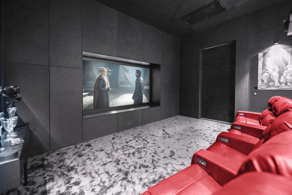 تصویری از سینما خانگی با صندلی‌های راحتی قرمز، نمایش فیلم از یک صفحه نمایش بزرگ و دکوراسیون مدرن.