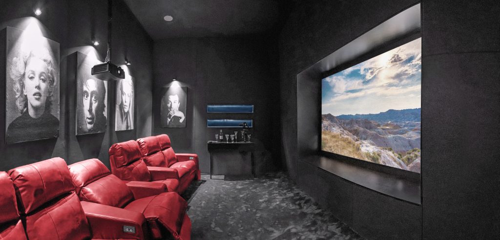 تصویری از سینما خانگی با صندلی‌های راحتی قرمز، نمایش فیلم از یک صفحه نمایش بزرگ و دکوراسیون مدرن.