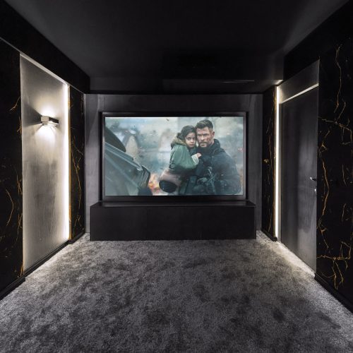 تصویری از راهرو سینما خانگی با نورپردازی زیبا، دیوارهای مرمر و نمایش فیلم سیاه‌وسفید از دو شخصیت سینمایی معروف.